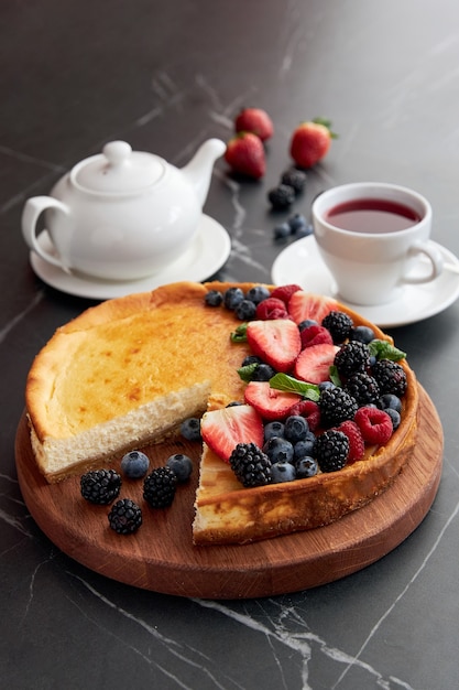Kuchen mit Beeren mit einem abgeschnittenen Stück mit einer Tasse Tee und Teekanne Erdbeeren Brombeeren Blaubeeren