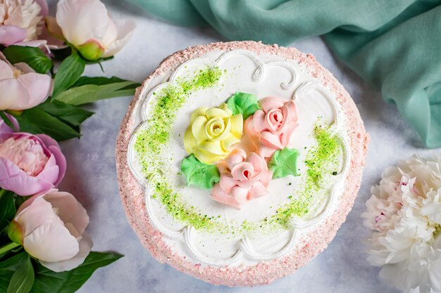 Kuchen mit Blumen in Pastellfarben auf Holztisch mit Pfingstrosen verziert