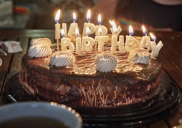 Kuchen mit der Aufschrift Happy Birthday mit brennenden Kerzen.