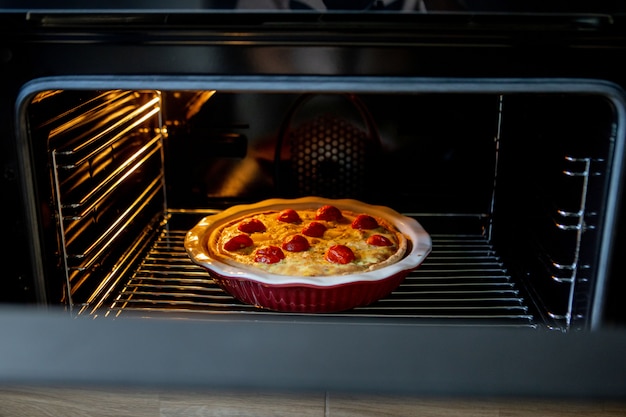 Kuchen mit Hühnchen und Tomaten liegt auf einem Backblech im Ofen.