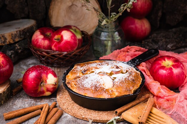 Kuchen mit Äpfeln, die eine Eisenpfanne füllen. Reife Äpfel auf einem Holztisch.