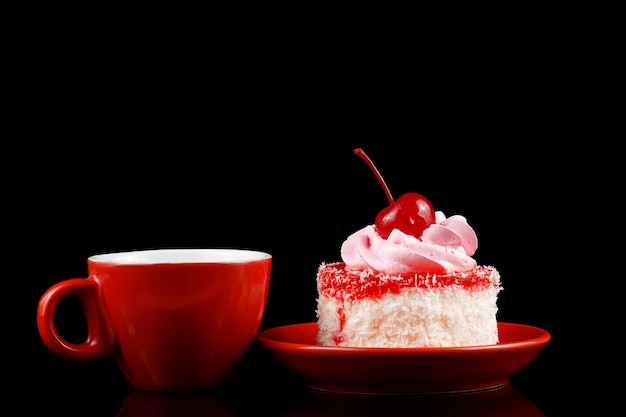 Kuchen mit Sahne und Kirsche auf einer roten Untertasse und Kaffee