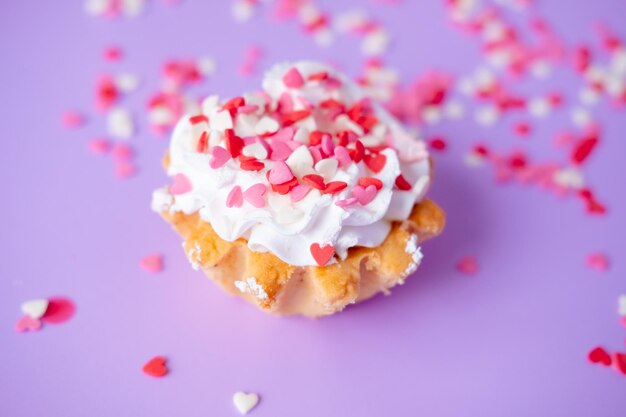 Kuchen mit Schlagsahne, gespickt mit kleinen Herzen auf violettem Hintergrund Valentinstag- und Geburtstagskonzept