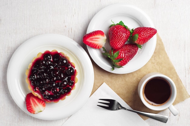 Kuchen mit schwarzen Johannisbeeren, Erdbeere und Kaffeetasse auf dem Tisch, Ansicht von oben