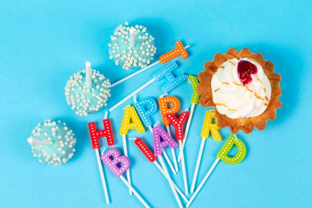 Kuchen und Cupcakes mit regenbogenfarbenen Geburtstagskerzen mit den Worten Happy Birthday