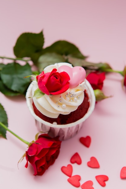 Kuchenrosen und -herzen auf einem Rosa. Schokoladenkleine kuchen verziert mit Sahnerose