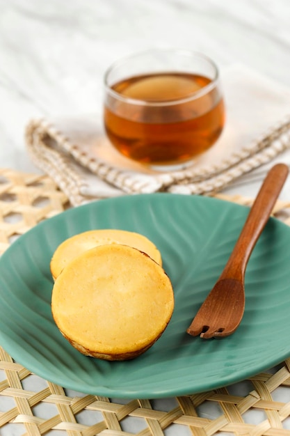 Foto kue lumpur o mud cake pastel tradicional indonesio hecho de patata de textura dulce y suave servido en un plato de cerámica verde con té