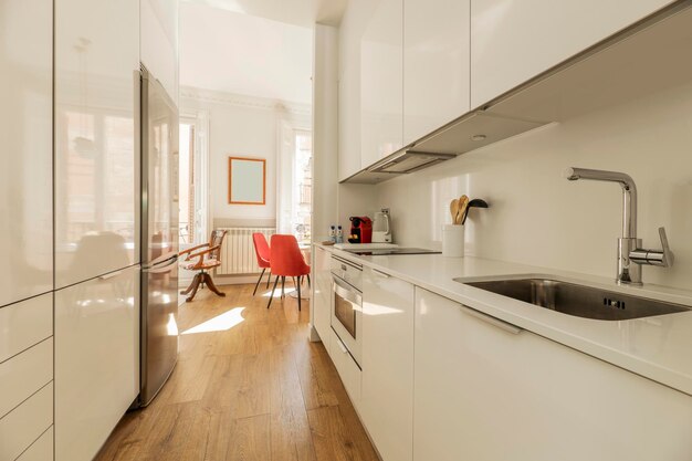 Küche mit glänzend weißen Holzschränken, Arbeitsplatten aus weißem Stein, weißen Einbaugeräten und Hartholzböden aus Kastanienholz und Zugang zu einem hellen Wohnzimmer