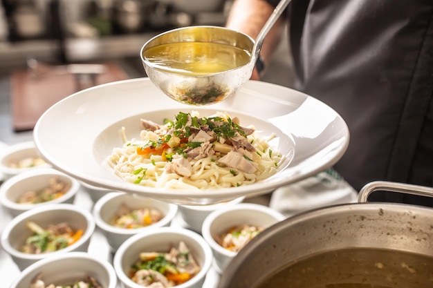 Küchenchef gießt Brühe in eine Hühnersuppe mit Nudeln, Fleisch und Gemüse