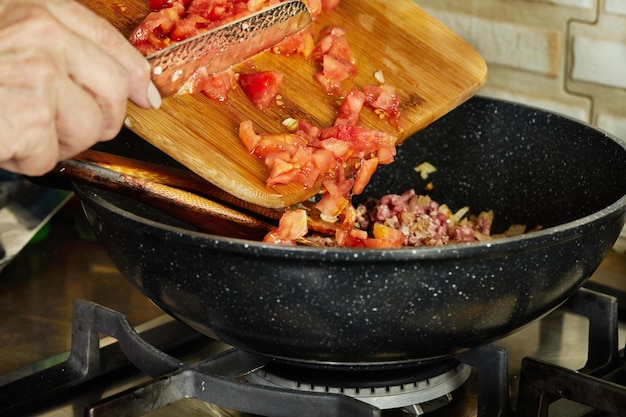 Küchenchef gießt gehackte Tomaten vom Holzbrett in die Pfanne