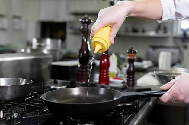 Küchenchef gießt Olivenöl aus einer Flasche in eine Pfanne