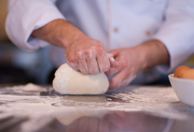 Küchenchef Hände bereiten Teig für Pizza auf mit Mehl bestreuten Tisch Nahaufnahme
