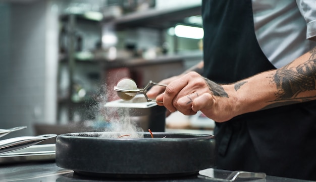 Küchenchef Hände mit mehreren Tattoos, die frisch gekochte Pasta Carbonara eine Würze verleihen