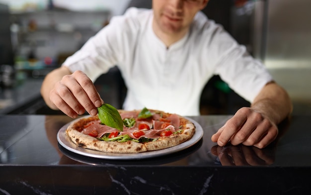 Küchenchef Pizzaiolo dekoriert Pizza mit frischen Oregano-Blättern