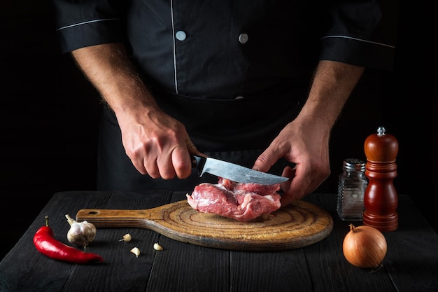 Küchenchef schneidet Fleisch mit einem Messer in der Küche und bereitet Essen zu Gemüse und Gewürze auf dem Küchentisch