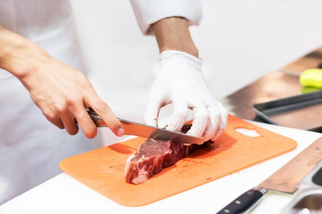 Küchenchef schneidet frisches rohes Fleisch mit einem Messer in der Küche Küche schneidet Rindfleisch auf einem Brett