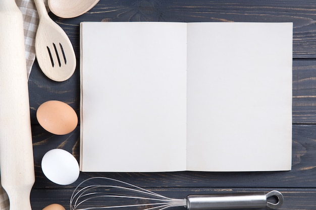 Küchengeräte und offenes leeres Weißbuch auf Holztisch