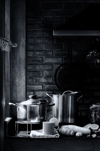 Foto küchenraum mit geschirr, herd, abzugshaube und ziegelwand mit einer tasse zitronentee mit dampf und dampf. konzept des chef- oder kochliebhaberlebens. retro schwarzweiss-bild.