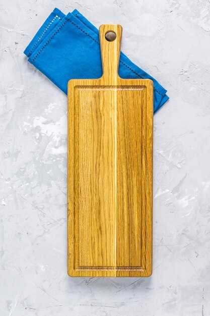 Küchenutensilien-Hintergrund Holzschneidebrett mit blauer Serviette auf hellgrauer Tischoberfläche