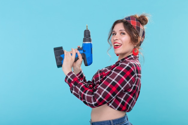 Kühle positive junge Frau in einem karierten Hemd, das einen Schraubenzieher hält, der auf einer blauen Oberfläche aufwirft