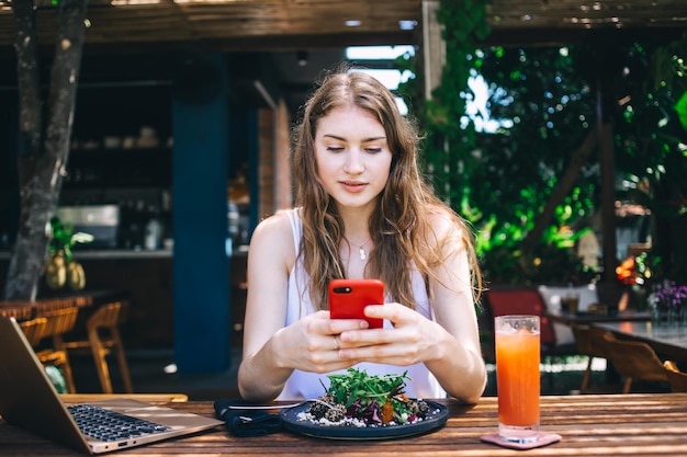 Kühlende weibliche Nachrichtenübermittlung am Telefon im Café