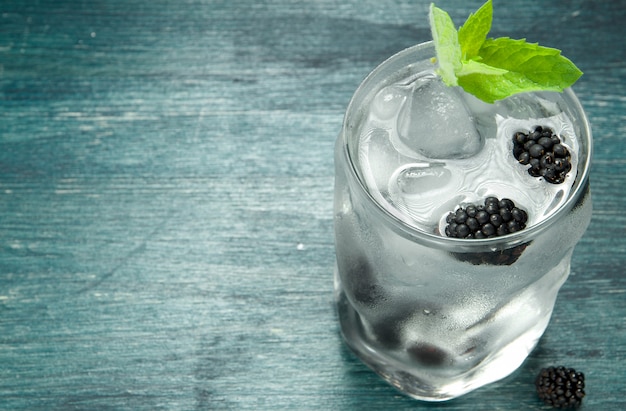 Kühles Süßwasser in einem Glas mit Brombeerbeeren, Eiswürfeln und Minze auf einem Holztisch.