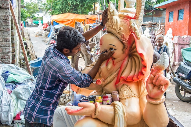 Künstler, der eine Statue herstellt und einem Idol des hinduistischen Gottes Lord Ganesha in einer Künstlerwerkstatt für das Ganesha-Fest den letzten Schliff gibt.