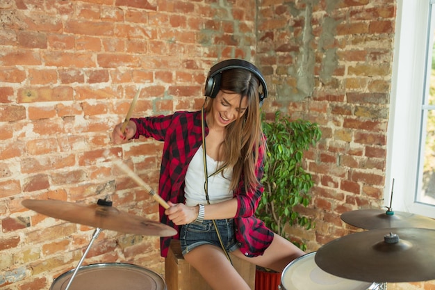 Foto künstler. heimmusikstudio, schöne frau, die musik aufnimmt, singt und schlagzeug spielt, während sie im loft-arbeitsplatz oder zu hause sitzt. konzept von hobby, musik, kunst und kreation. erste single erstellen.