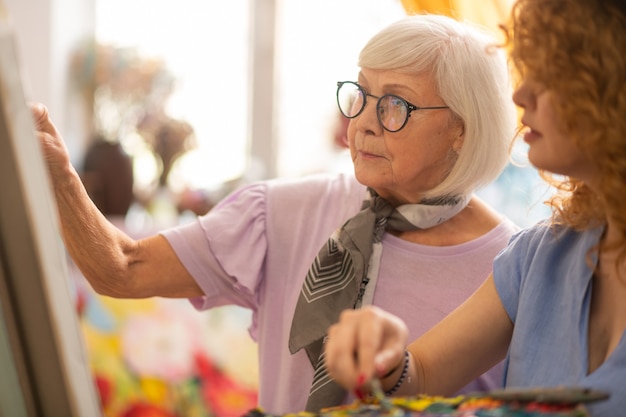 Künstler mit Brille. Alter Künstler, der eine Brille trägt, die ihrem lockigen Schüler mit Bild hilft