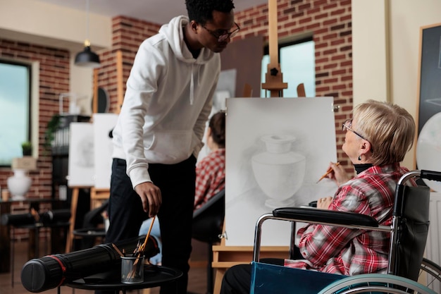 Künstlerische Lehrerin erklärt älteren Frauen mit Behinderungen die Zeichentechnik, die beim Illustrationsprozess im Kreativitätsstudio zusammenarbeiten. Verschiedene Menschen nehmen an Kunstkursen teil, um sich persönlich weiterzuentwickeln