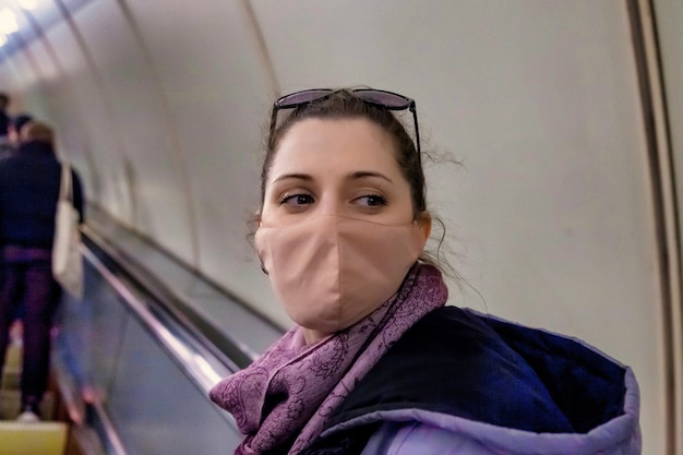 Künstlerisches Rauschfilmkorn. Junge Frau in steriler medizinischer Schutzmaske an der U-Bahn-Rolltreppe. Frauen tragen Gesichtsmaske, schützen vor Virusinfektion, Ausbruch und Epidemie in Quarantänestadt