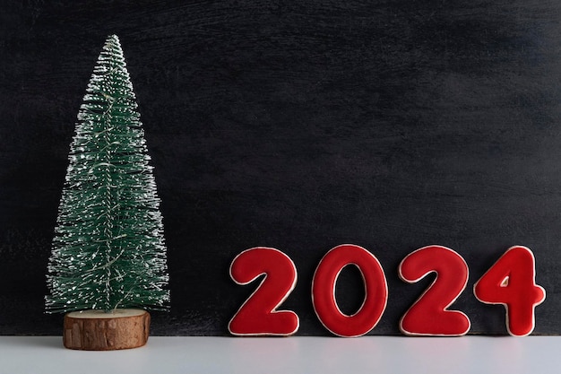 Künstlicher Weihnachtsbaum und rote Zahlen 2024 auf schwarzem Hintergrund Neujahrskonzept