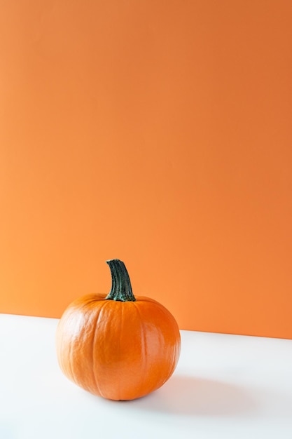 Kürbis auf weißer Tabelle über orangefarbenem Hintergrund. Erntedankfest oder Halloween-Zeit