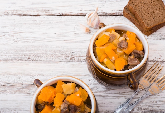 Kürbis, Fleisch, Kartoffeln und Gemüse in einem Keramiktopf auf einem weißen Holztisch gebacken.