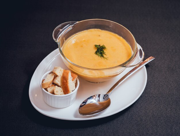 Kürbis-Karotten-Suppe mit Sahne und Petersilie auf dunklem Hintergrund.