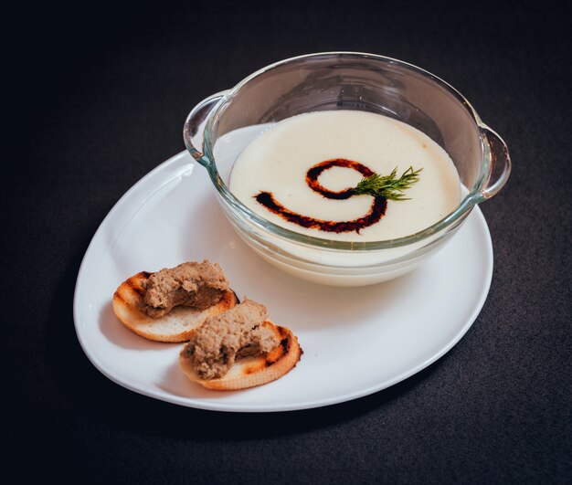 Kürbis-Karotten-Suppe mit Sahne und Petersilie auf dunklem Tisch