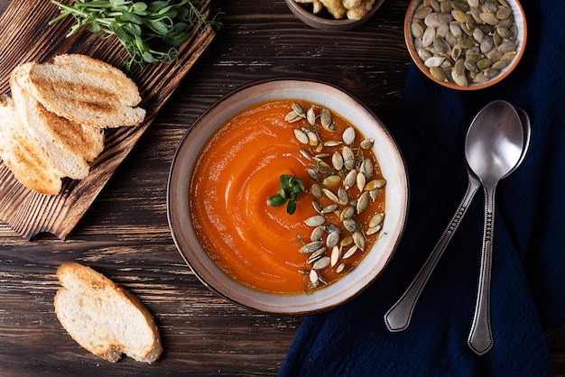 Kürbiscremesuppe auf Holzhintergrund, herbstliche vegane pürierte Suppe im rustikalen Stil, Draufsicht.