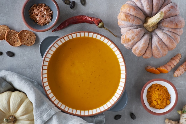 Kürbiscremesuppe in der gestreiften keramischen Schüssel umgeben durch Bestandteile, Textraum