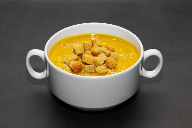 Kürbiscremesuppe mit crackern auf einem dunklen hintergrund. kürbiscremesuppe mit crackern und sesam in einer weißen bouillon auf einem dunklen hintergrund