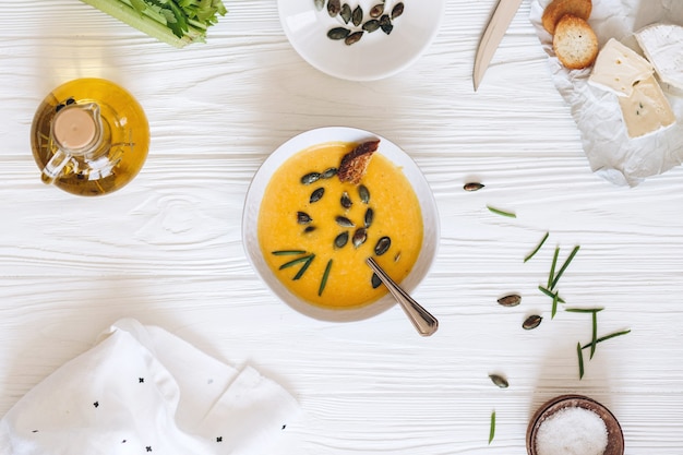 Kürbiscremesuppe mit Käse und Zwiebeln auf einem weißen Brett. Stillleben flach liegen