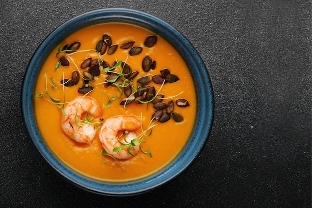 Kürbiscremesuppe mit Samen und Garnelen auf dunklem Betontisch und mikrogrüner Draufsicht