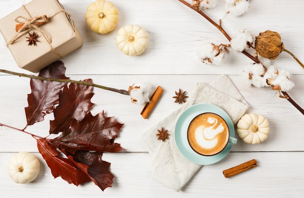 Kürbisgewürz Latte. Kaffeetasse mit Schaum, Zimtstangen, roten Eichenblättern und kleinen gelben Kürbissen. Heiße Getränke im Herbstherbst, Café- und Bar-Konzept, Draufsicht