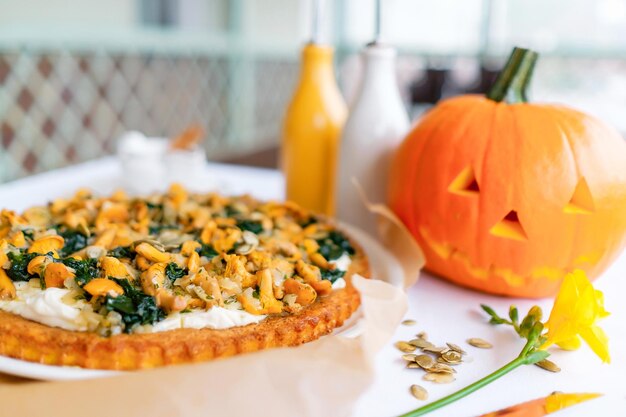 Kürbiskuchen mit Pfifferlingen Ein geschnitzter Kürbis im Hintergrund Traditionelles Halloween-Gericht serviert auf einem Tisch mit einer weißen Tischdecke Draufsicht