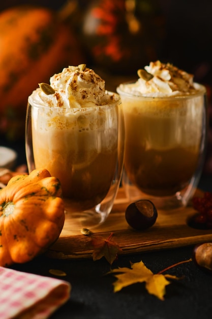 Kürbislatte mit Schlagsahne in einer Brille im Stil von dunklem Essen. Herbst Heißes würziges Getränk für