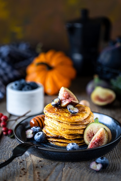 Kürbispfannkuchen mit Sirup oder Honig, Leinsamen, Feigen, Blaubeeren in einem dunklen Teller auf dem Tisch, selektiver Fokus, Kopierraum