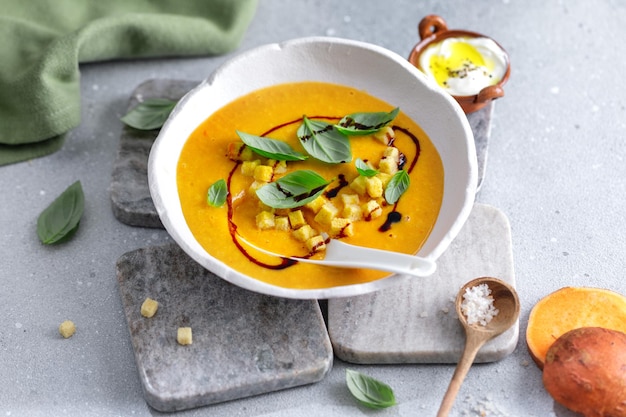 Kürbispüreesuppe mit Croutons und Basilikum, serviert in einer Schüssel auf dem Tisch