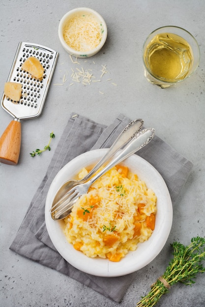 Kürbisrisotto mit Thymian, Knoblauch, Parmesan und Weißwein auf grauer Beton- oder Steinoberfläche. Selektiver Fokus. Rustikaler Stil. Draufsicht.