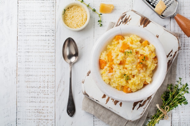 Kürbisrisotto mit Thymian, Knoblauch, Parmesan und Weißwein auf hellem Holzhintergrund Rustikaler Stil