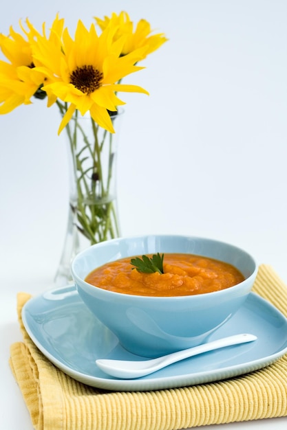 Kürbissuppe in einem blauen Teller und einem Strauß gelber Blumen