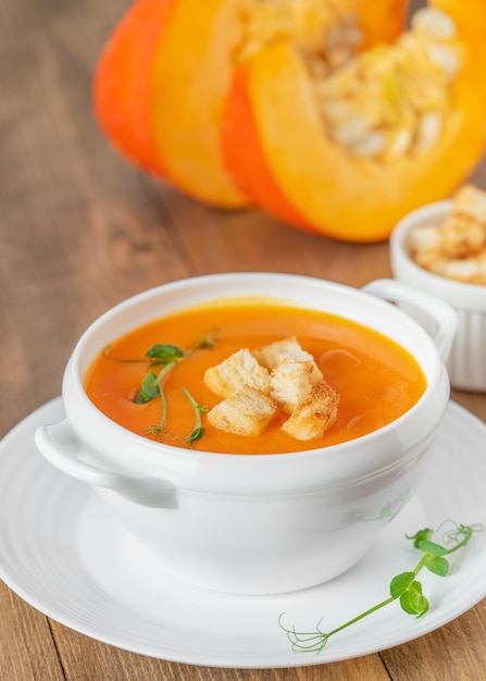 Kürbissuppe mit Croutons in weißer Schüssel auf Holzhintergrund Nahaufnahme